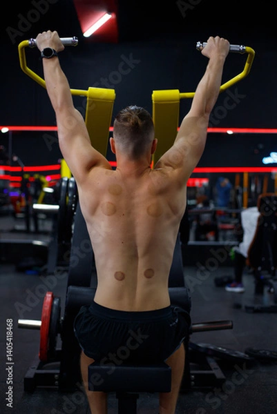 Fototapeta Caucasian guy doing lat pulldowns on a machine in the gym