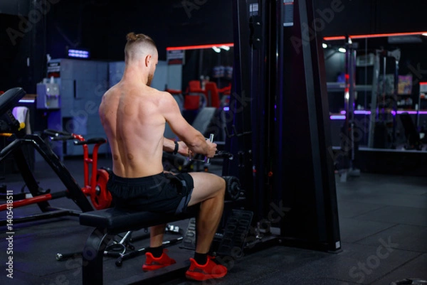 Fototapeta Caucasian guy doing lat pulldowns on a machine in the gym