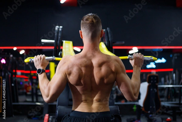 Fototapeta Caucasian guy doing lat pulldowns on a machine in the gym