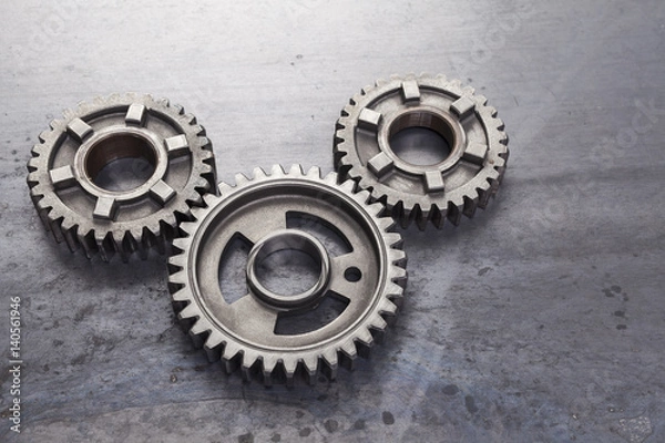 Fototapeta Grupa solidnych metalowych kół zębatych jest połączonych ze sobą na grungy stalowym tle. Ten zestaw przemysłowych kół zębatych może służyć do reprezentowania koncepcji pracy zespołowej.