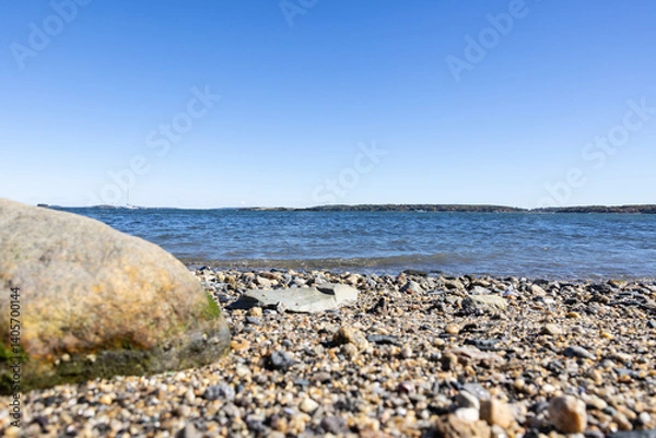 Obraz Photograph of One large boulder on a rocky pebble beach on bright sunny day and calm wavy ocean water