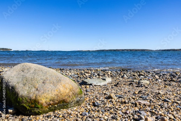 Fototapeta Photograph of one large boulder rock on a pebble beach shore deep blue calm ocean water.