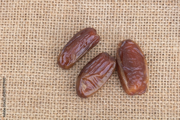 Fototapeta Three dates on a burlap background, top view, close-up