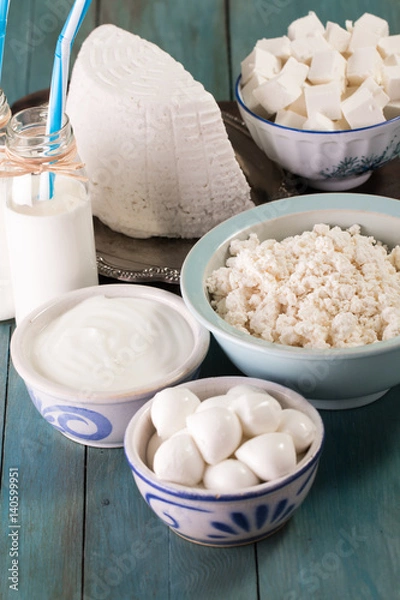 Obraz tasty healthy dairy products on a table on a blue background: sour cream, cottage cheese, mozzarella cheese, butter,ricotta and milk in a bottle
