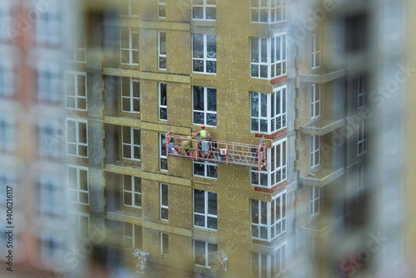 Fototapeta Worker insulates the facade of a high-rise building