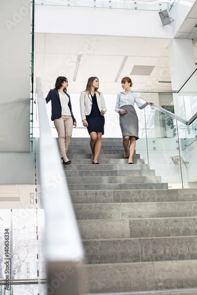 Fototapeta Businesswomen conversing while moving down steps in office