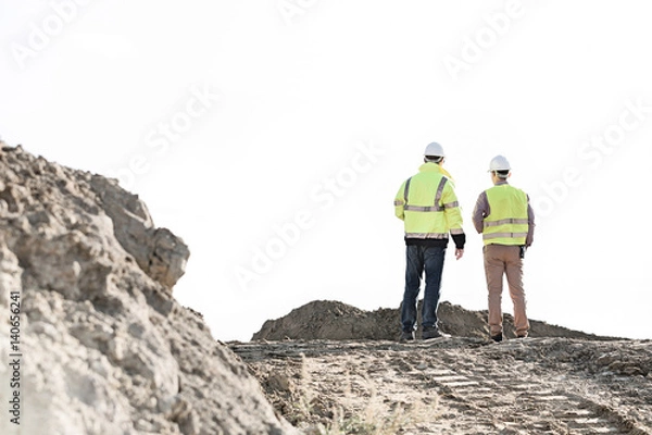 Fototapeta Rear view of supervisors standing at construction site against clear sky