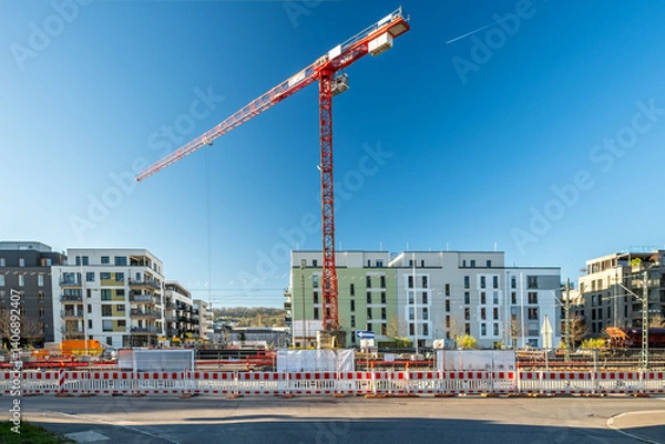 Obraz Construction site with cranes and fence in front of modern residential buildings