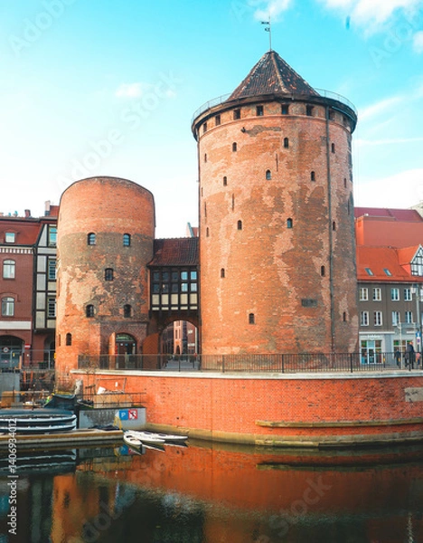 Fototapeta Picturesque view of the medieval Prison Tower and Torture Tower on the waterfront in Gdańsk, Poland. The scene features charming Hanseatic townhouses.