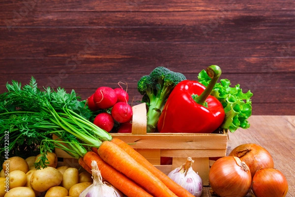 Fototapeta Vegetables. Potatoes, carrot and red pepper. Lettuce salad, garlic and brocoli. Onion and radish. Wooden basket on rustic table.