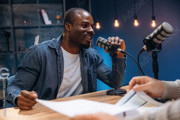 Fototapeta Sitting by the table. Two radio presenters recording an audio broadcast in a studio