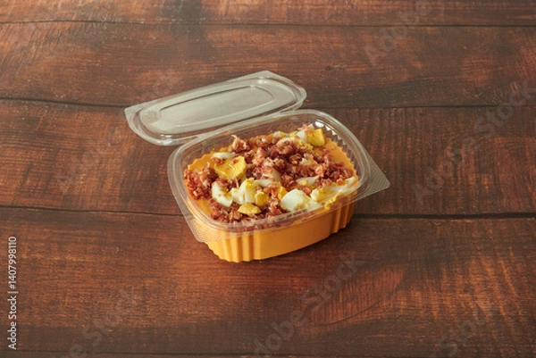 Fototapeta A container of food with a lid on top. The lid is plastic. The food is yellow and has bacon and eggs in it
