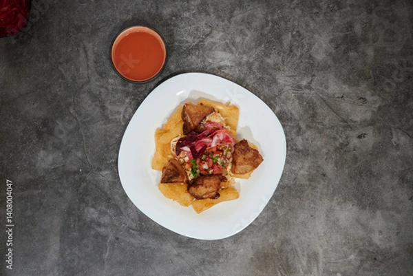 Obraz A plate of food with a sauce on the side. The plate is white and has a variety of food on it