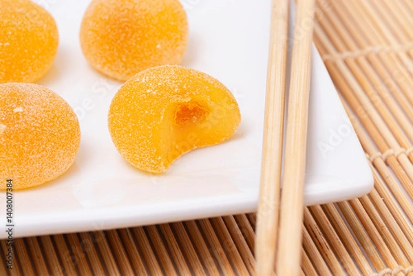 Fototapeta Sweet Mango Flavored Fruit Mochi on a Bamboo Mat with Chopsticks