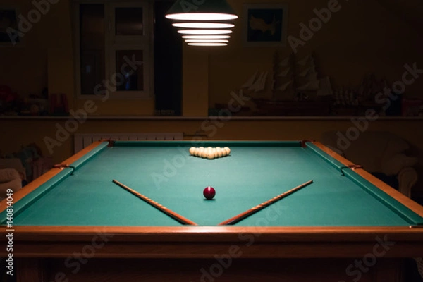 Fototapeta Billiard table with balls and cues in the light of the lamps