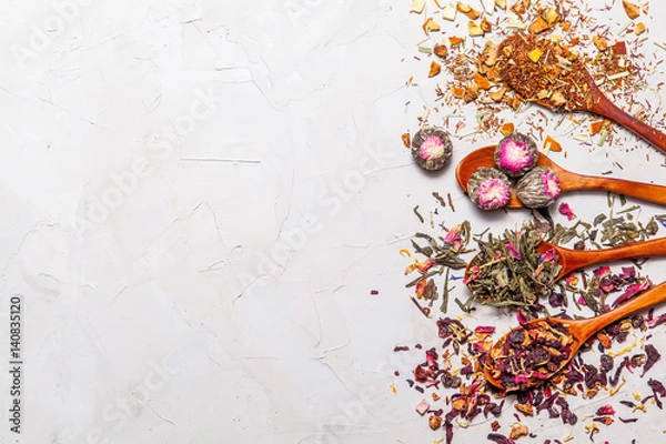 Fototapeta Dry tea in wooden spoons on grey background, top view. Leaves of red, fruit , green and black tea with  fruits and spices