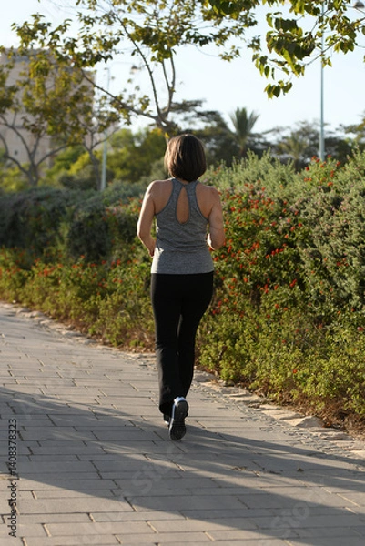 Obraz Active middle-aged woman doing stretching and jogging outdoors at sunset