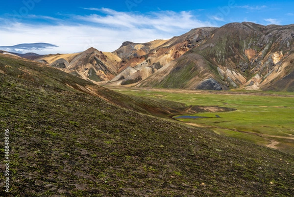 Fototapeta A panorama scene of colorful volcanic landscape with a moss-covered slope leading to a green valley and brown mountains along the Laugavegur trail, Iceland