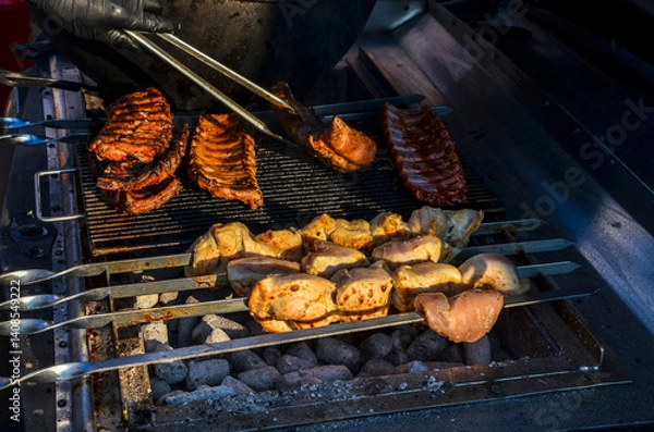Fototapeta Selection of meats, including kebabs and ribs, are being grilled on a barbecue during a warm evening, showcasing a tasty barbecue dish preparation
