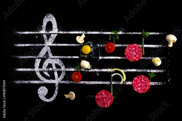 Fototapeta Pizza music. Treble clef made of flour on a black background and notes - salami, mozzarella cheese, tomatoes and mushrooms