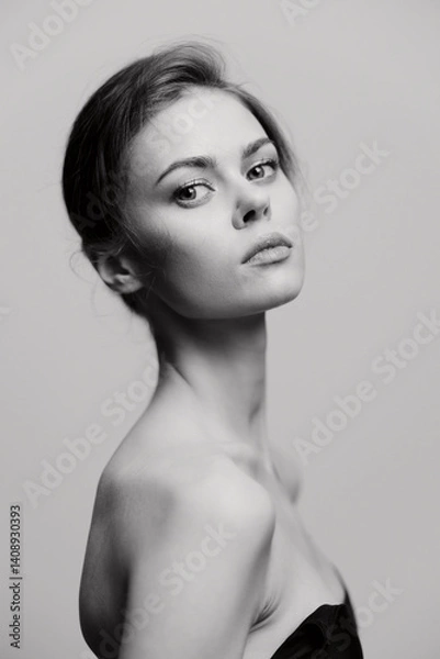 Obraz Elegant woman posing in a black strapless top against a soft gray background, exuding confidence and grace. Portrait emphasizing beauty and style.