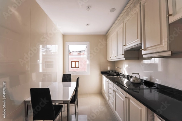 Fototapeta Modern kitchen interior. Design of a narrow kitchen with a small table and three chairs. Comfortable hob and modern furniture. Marble floors, tiles on the walls