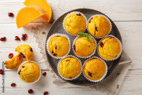 Fototapeta Autumn muffins with pumpkin puree, dried cranberries, orange zest and spices close-up in a plate on the table. Horizontal top view from above