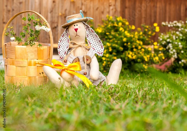 Fototapeta Easter toy rabbit with basket and colorful easter eggs sitting on natiral grass. Happy Easter greeting concept