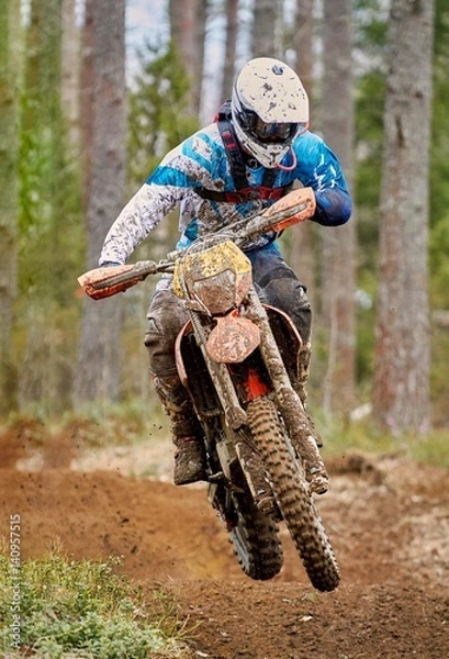 Obraz Motocross driver jumping with the bike at high speed on the race track