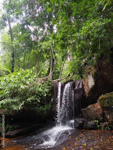 Fototapeta Small waterfall in a lush tropical forest surrounded by rocks and dense greenery