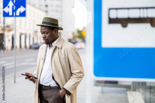 Fototapeta Man using his mobile phone at a bus stop in the city

