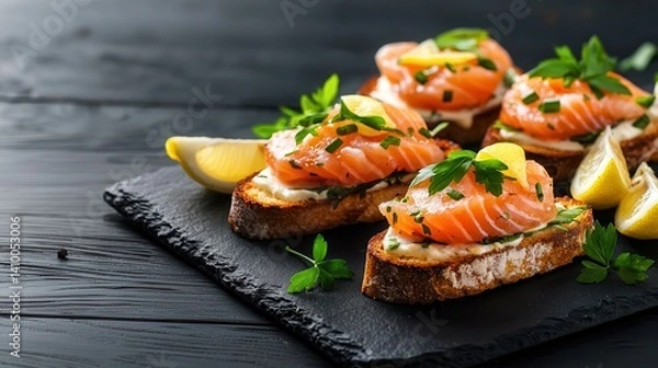 Fototapeta Bruschetta and fish tartare appetizer Gourmet salmon toast with herbs and lemon on a slate platter.