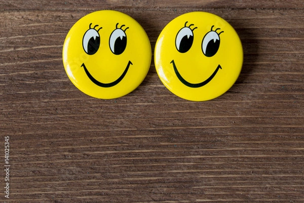Obraz Two yellow buttons with smiley faces on a wooden background. Close up