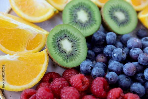 Fototapeta Closeup of colorful assorted fresh fruits, kiwi, bluerberryes, red-raspberries and orange slices on a plate. Photographed in natural light.Selective focus.