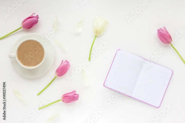 Fototapeta Flowers composition. Woman's workspace wiht notebook, cup of coffee white and lilac tulip, pen on white background. Flat lay, top view