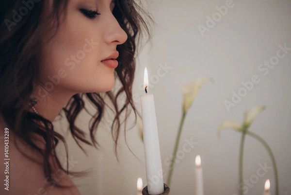 Fototapeta Profile view of a woman near candle and flowers in soft moody light