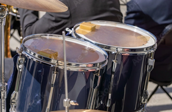 Obraz Close-up of a jazz musician's drum kit. The drums have clear membranes, secured with tape to muffle the sound. In the background, musicians in elegant outfits can be seen. Live performance