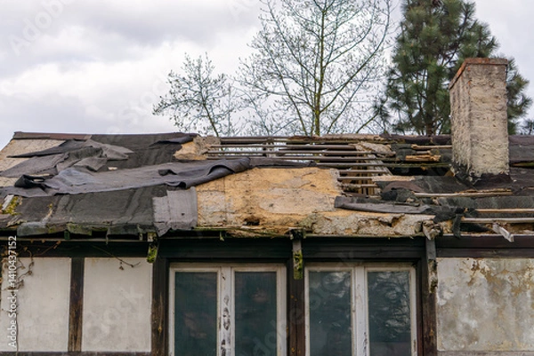 Obraz destroyed roof of an old building. You can see torn roofing felt, exposed roof beams and fragments of destroyed insulation. abandoned ruined house.