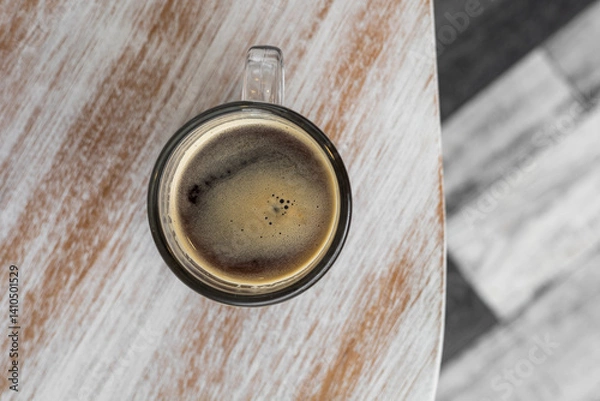 Obraz A coffee mug sits on a wooden table with blended cream and honey shades, highlighting natural grains and a cozy, inviting atmosphere.

