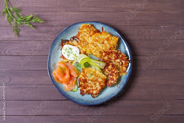 Fototapeta Hash browns with smoked salmon, cucumbers and yogurt. Vegetable fritters, latkes, potato cakes. Vegetable pancakes. High angle view