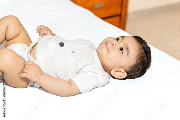 Fototapeta baby lying in bed looking at the ceiling with a small subtle smile