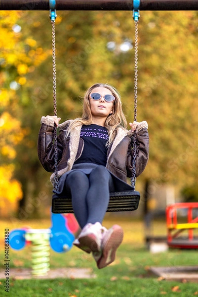 Fototapeta Happy laughing girl with sunglasses on a swing swinging on a playground. Happy childhood, family vacation in park