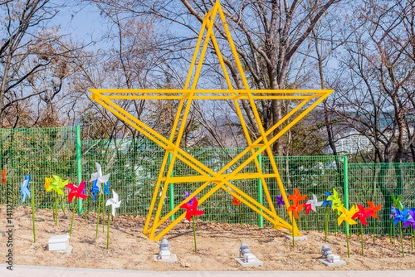 Fototapeta Yellow star structure surrounded by colorful pinwheels against a backdrop of trees.