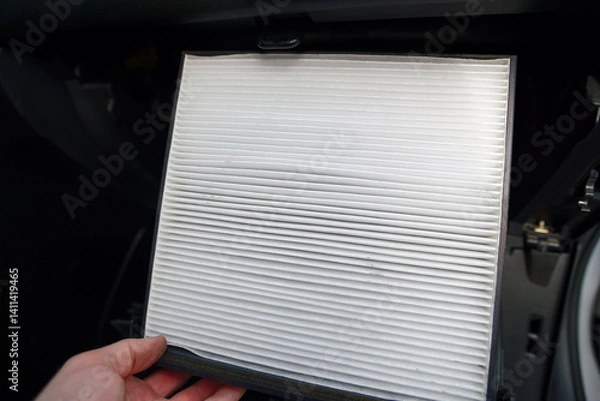 Fototapeta Hand with new clean cabin air filter, ready to install inside the glovebox of car as part of routine maintenance to improve air quality, ventilation. New cabin air filter installation. Selective focus
