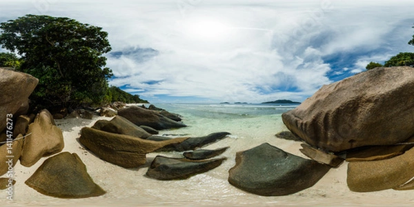 Fototapeta Smooth granite boulders rest on the sandy beach, with lush greenery in the background and clear ocean waves. La Digue, Seychelles. 360 Degree view.