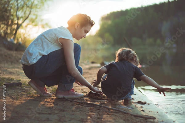 Obraz Мама и сын на берегу озера компает песок на закате