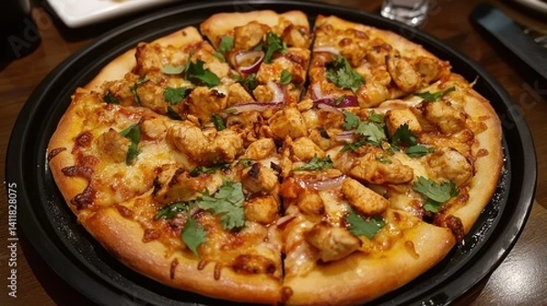 Fototapeta A delicious chicken pizza with melted cheese on a black plate, presenting a savory and satisfying meal.