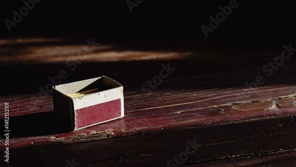 Fototapeta A small box of matches sits on a wooden table. The box is empty and the matches are not lit. The image has a simple and minimalistic feel to it, with the focus on the box of matches