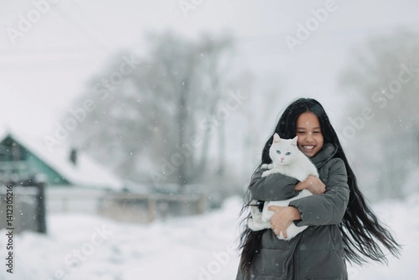 Obraz A girl with a white cat stands joyfully under the snow
