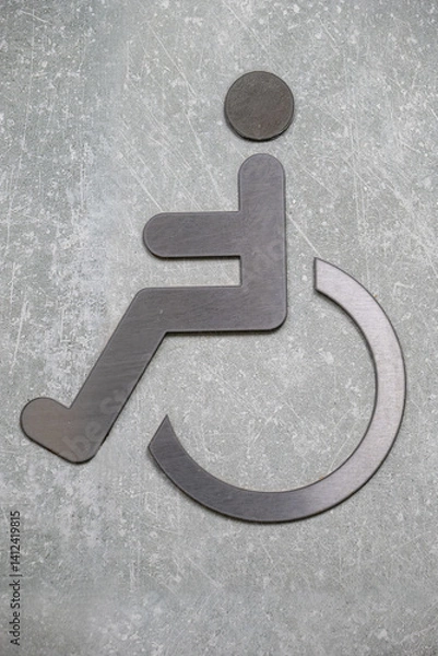 Fototapeta Metal wheelchair accessibility symbol on textured concrete wall. Close-up sign icon. Disability and accessibility concept for banner, poster, and template design